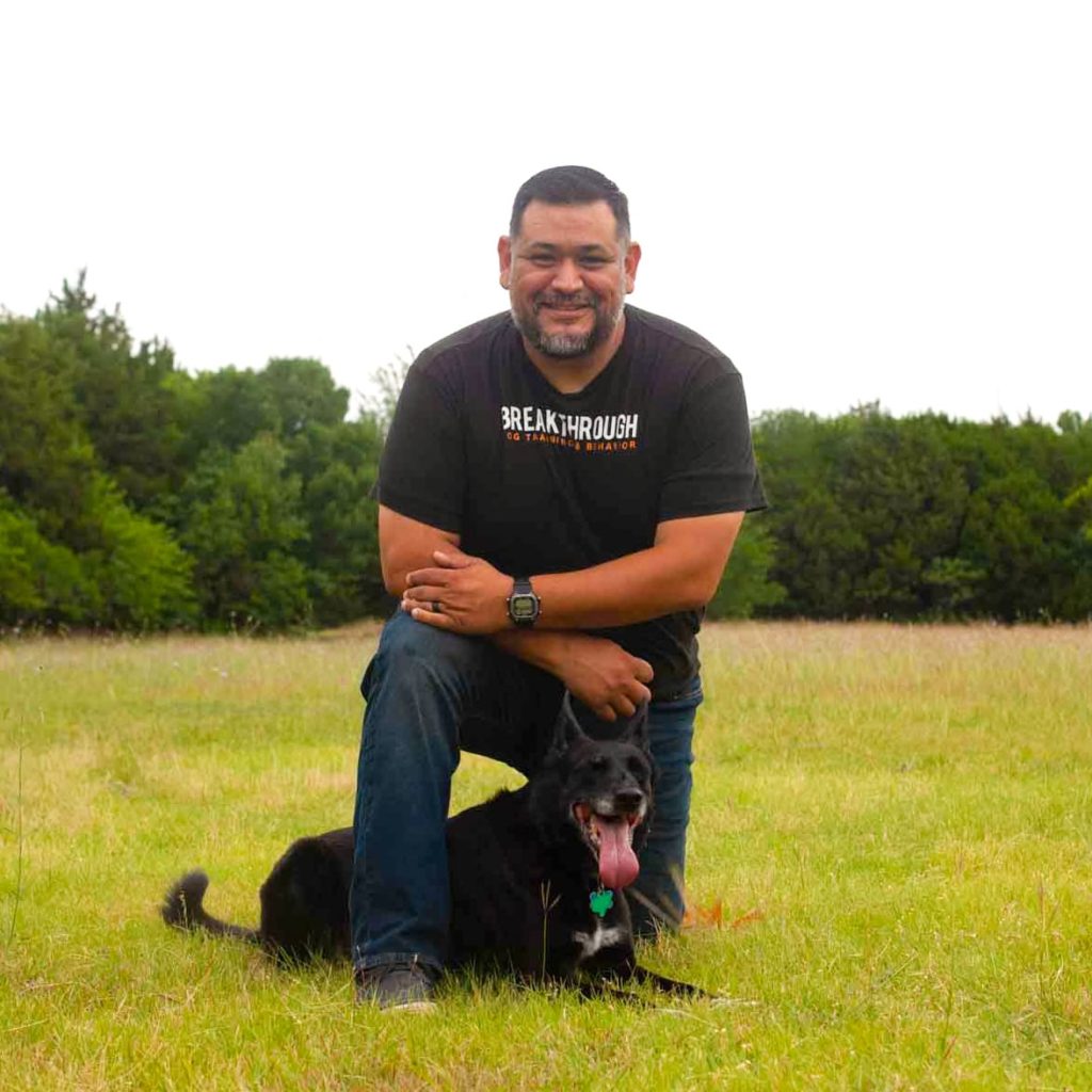 Photo of Eli Vega. dog trainer, with black dog in a park